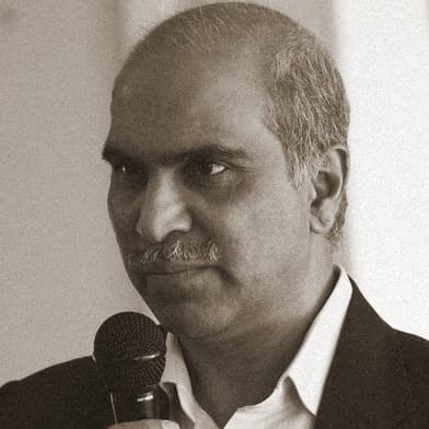 Portrait of Ravindra Gadgil, OMPEG Core Group, speaking into a microphone.